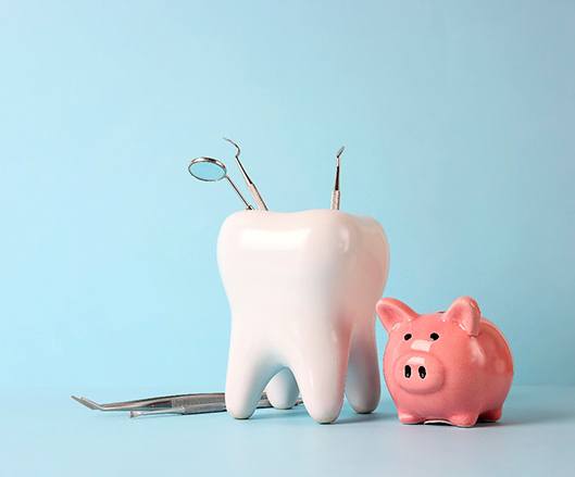 Pink piggy bank and tooth model with medical instruments on blue background.