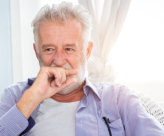 Man in need of dental implant tooth replacement covering mouth