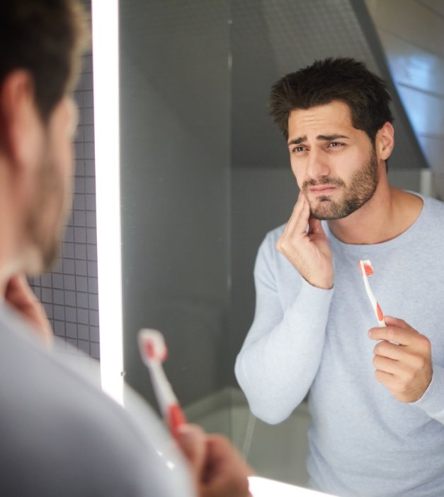 Man in need of emergency dentistry holding cheek after brushing teeth