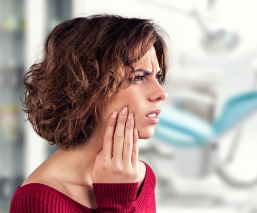 Woman holding cheek during emergency dentistry visit