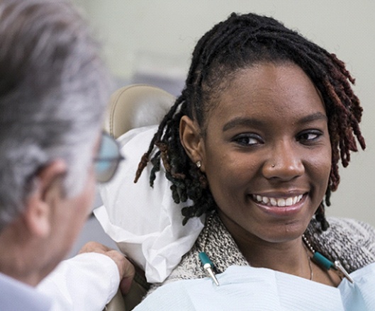 a person sitting in a treatment chair and speaking with their dentist