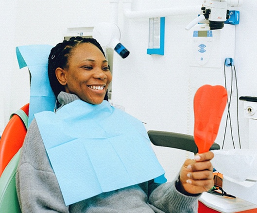 Woman looking in dental mirror after full mouth reconstruction.