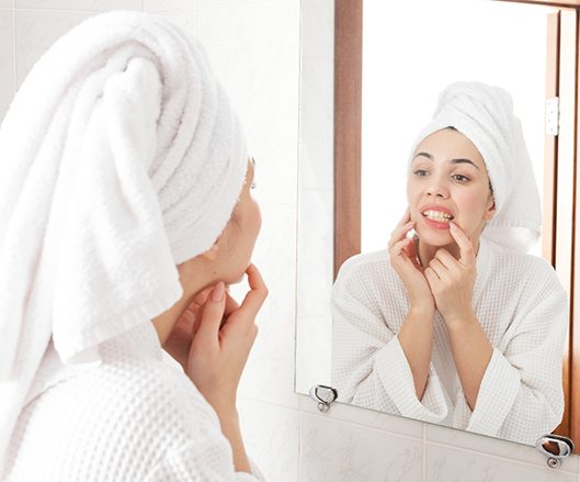 Woman in white robe looking at gums in reflection