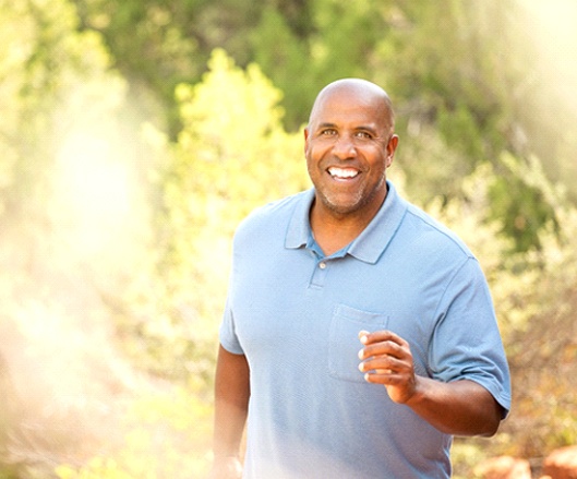 A middle-aged man taking a walk and smiling after receiving his implant dentures