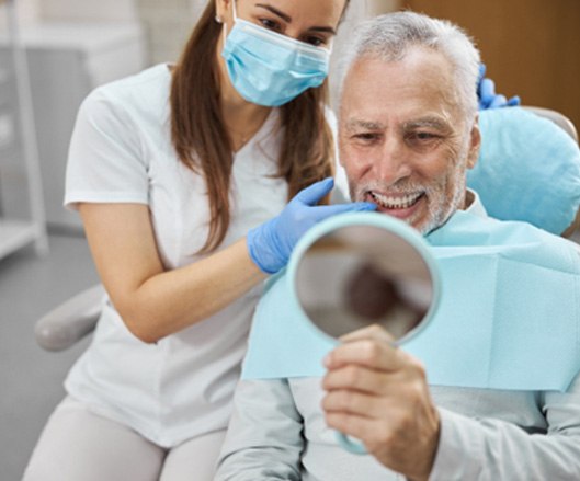 An older man admiring his new dental implant in a hand mirror