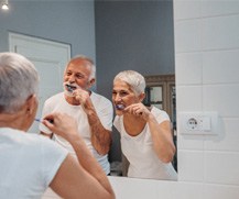 An older couple brushing their teeth in front of a bathroom mirror