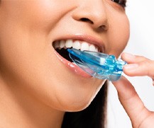 A smiling woman placing a mouthguard in her mouth