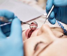 A dentist using dental tools to perform a checkup on a woman 
    
        