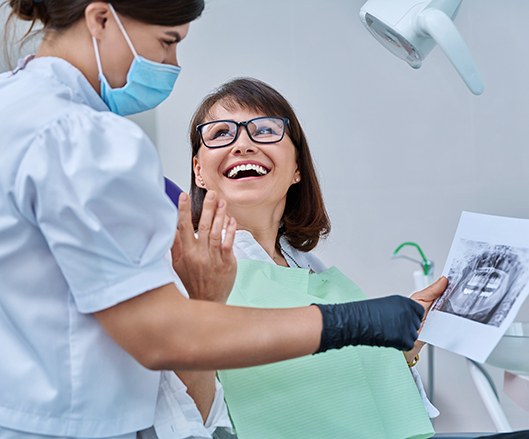 Woman smiling with dentist while reviewing X-ray