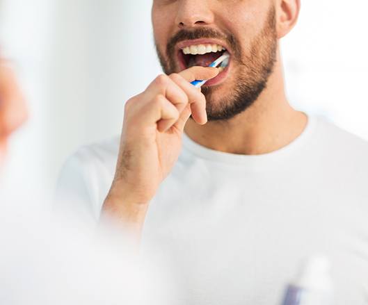 Man smiling while brushing his teeth