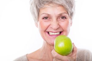 Woman with dental implants holding an apple. 