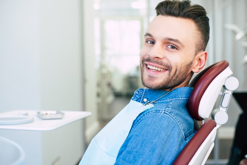 a young man wearing a denim shirt sits in the dentist’s chair smiling while waiting to learn if he’s a candidate for general anesthesia