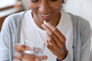 Woman holding glass of water about to swallow pill capsule